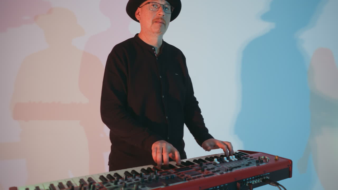 검은색 옷을 입은 키보디스트가 플러를 연주하고, 색 드레스를 입은 보컬리스트가 파란색 배경과 다채로운 조명과 그림자를 가진 배경에 나타납니다.