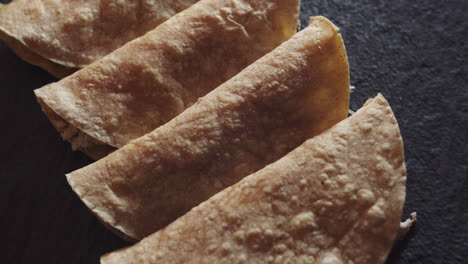 Beautiful-slow-motion-shot-of-a-group-of-4-tacos-or-Mexican-tortillas-with-chicken-placed-on-a-black-plate-and-dimly-lit