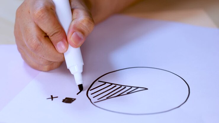 Close-up of hand sketching pie chart and geometric symbols on white paper with marker