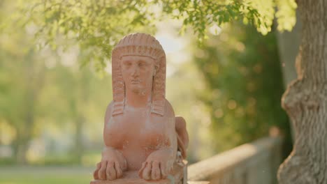 Terracotta-sphinx-statue-in-a-sunlit-garden,-surrounded-by-greenery