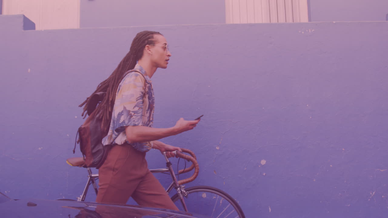 puntos de luz contra un hombre afroamericano que usa un teléfono inteligente mientras camina con su bicicleta