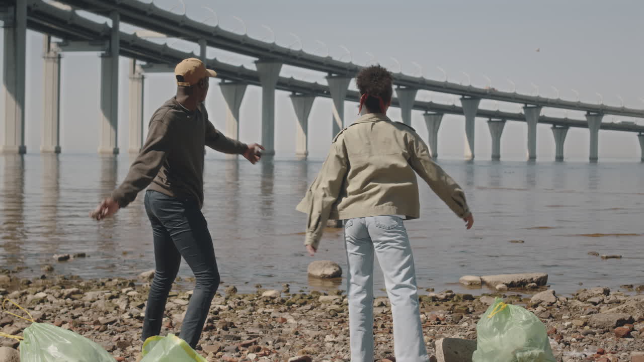 Couple Throwing Stones into Water after Cleaning Shore