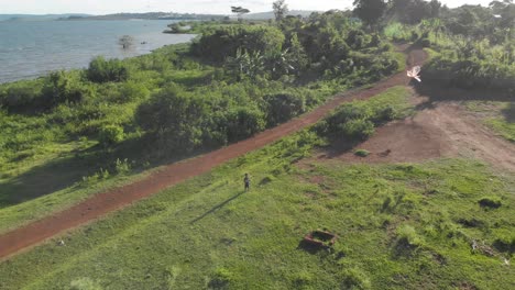 aerial shot orbiting around a young boy flying a kite by the shores of lake victoria in the evening sun