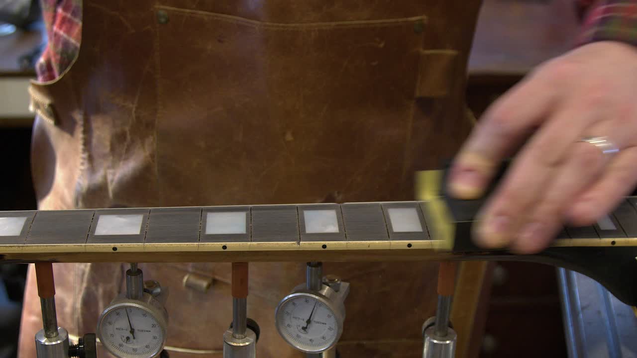 Técnico de guitarra lixa a escala de ébano em uma guitarra durante um reparo de retrasteamento.