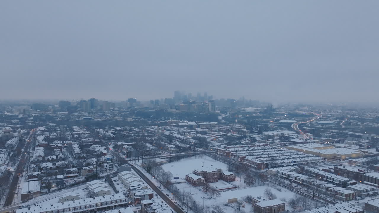 Aerial footage flying over in snow covered neighborhoods in West Philadelphia, Pennsylvania with a foggy downtown skyline in the background.