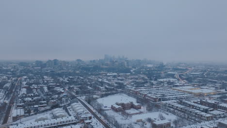 aerial footage flying over in snow covered neighborhoods in west philadelphia, pennsylvania with a foggy downtown skyline in the background.