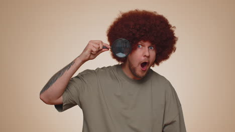 Investigator researcher man with magnifying glass near face, looking into camera with big zoom eye