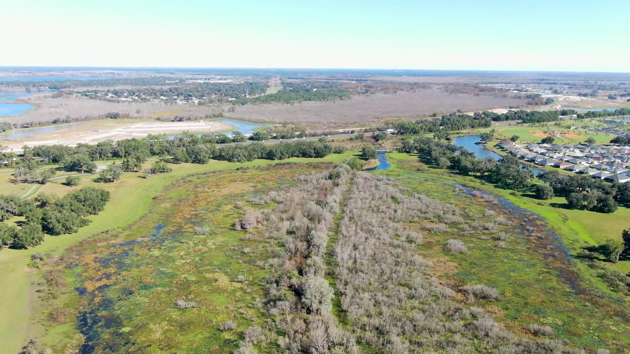 Ripresa aerea in movimento in avanti su una zona umida a The Villages, in Florida, che si sposta verso un'autostrada vicina con case residenziali visibili a est, evidenziando la natura e lo sviluppo fianco a fianco
