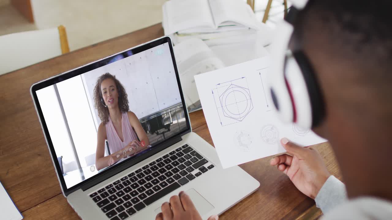 estudiante universitario afroamericano que sostiene notas mientras hace una videollamada en una computadora portátil en casa