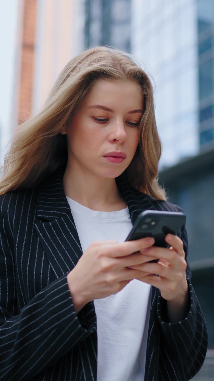 Giovane donna d'affari che usa lo smartphone all'esterno di un moderno palazzo per uffici