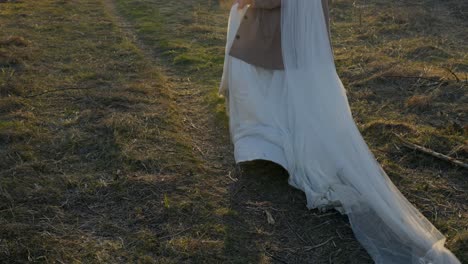 a bride in white dress runs past the camera in slow motion, glowing in sunset light, her face not in the frame.