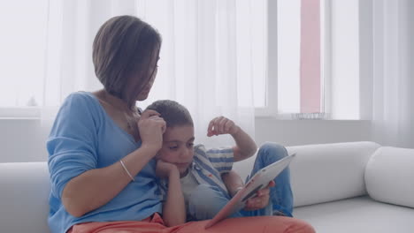 Happy-mother-and-little-son-reading-a-book-in-the-morning-together-in-the-living-room-at-home.-family-activity-concept.