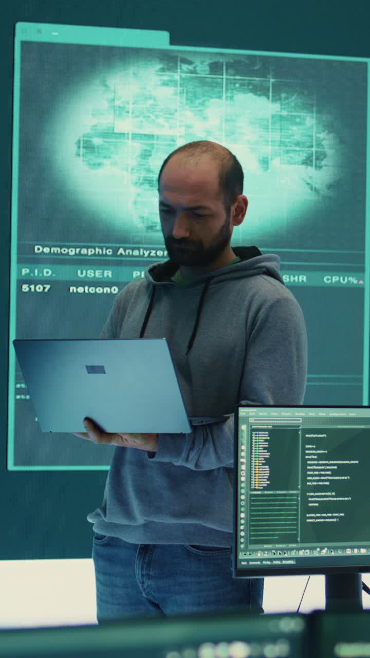 Man Working on Laptop in Dark Room with Multiple Screens