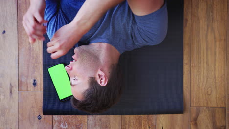 Overhead-View-Of-Man-Lying-On-Exercise-Mat-At-Home-Taking-Out-Wireless-Earphones-After-Workout