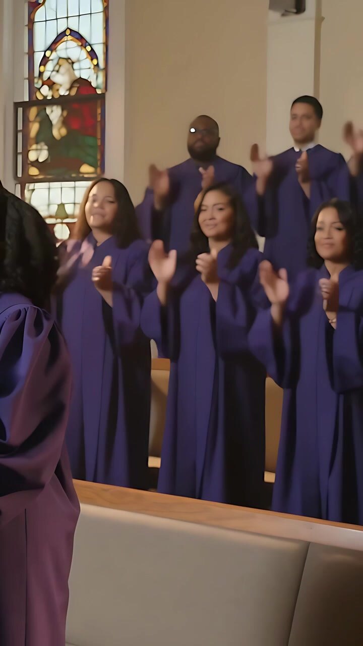 Video verticale: La telecamera si allarga mostrando un coro in abiti viola che applaude su delle pedane durante una funzione religiosa.