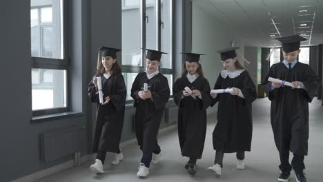 asian student with his mother walking in the corridor. they talk. the kid is wearing a mortarboard and holds a diploma.