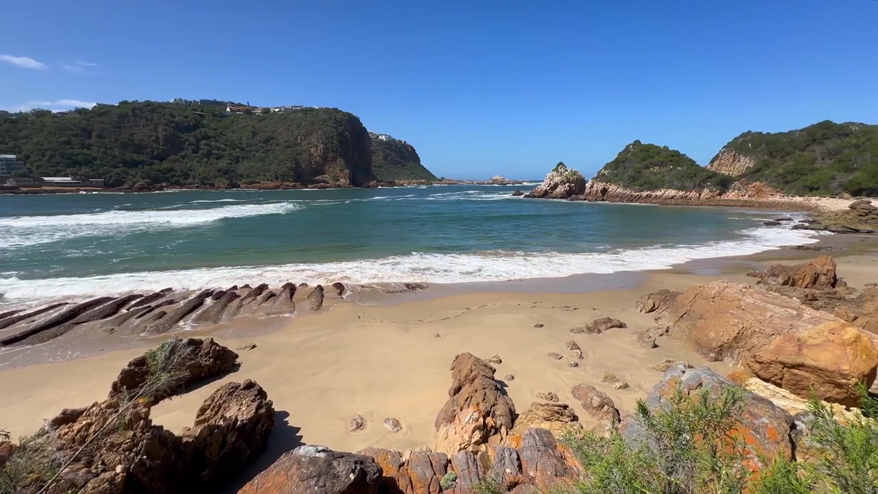 Panoramica a destra di Coffin Beach sotto un cielo azzurro e limpido a Knysna, Sudafrica