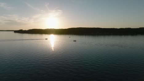 Orbiting-drone-shot-of-the-silhouettes-of-fishing-boats-and-pontoons-on-a-lake-at-sunset