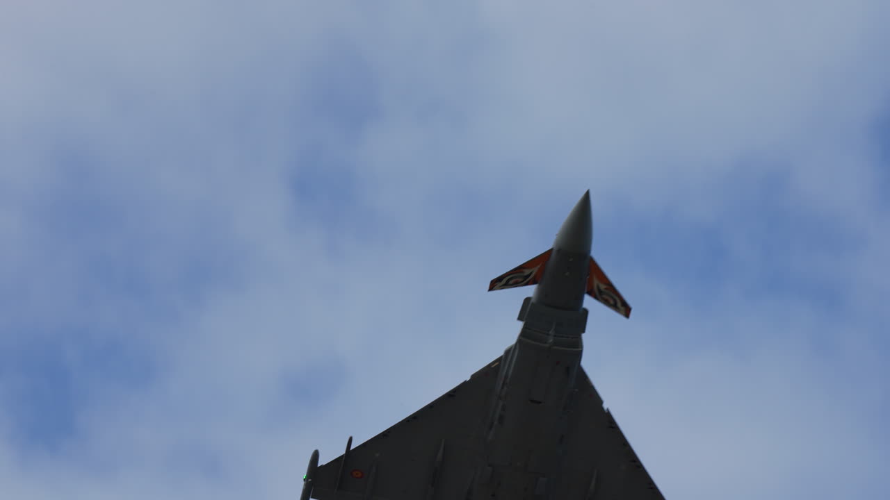 Military fighter jet seen from below during aerial stunt with decorated tail wings and visible details