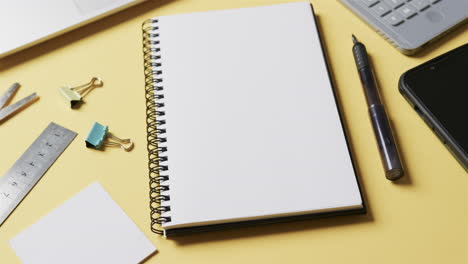 close-up van notebook, smartphone en schoolpapier op gele achtergrond, in slow motion
