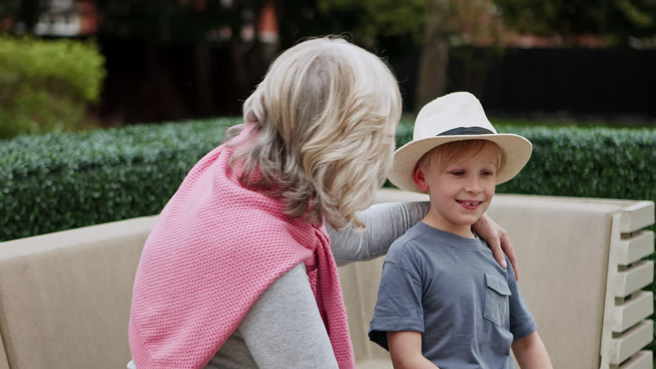 A grandmother adjusts a boy's hat in a garden