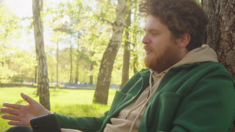 man using phone while dog playing in park