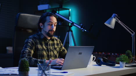 smiling man sitting at home office desk and typing on laptop keyboard,