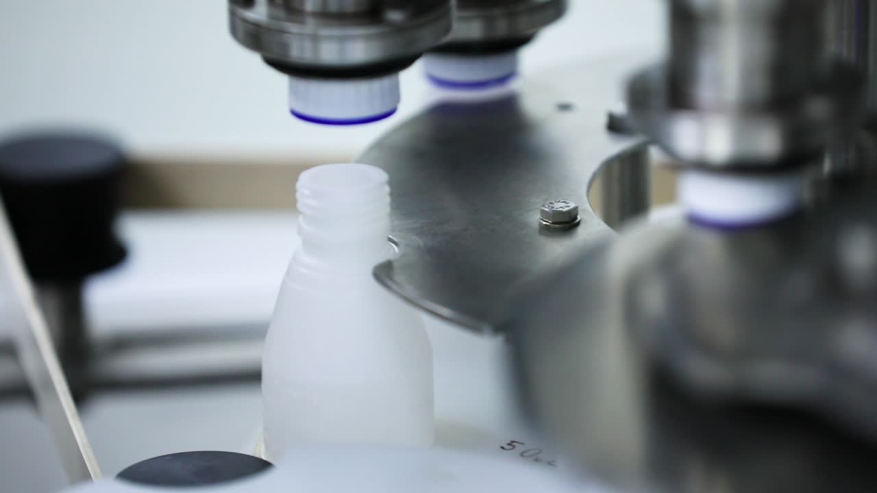 Bottle capping automatic machine. Cough syrup getting caps in automatic machine. Medical white bottle getting capped by a automatic machine.