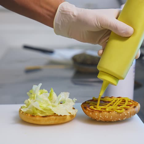 a hand in white gloves pouring sauce on toasted half of the bun. making a delicious hamburger. kitchen in restaurant. front video