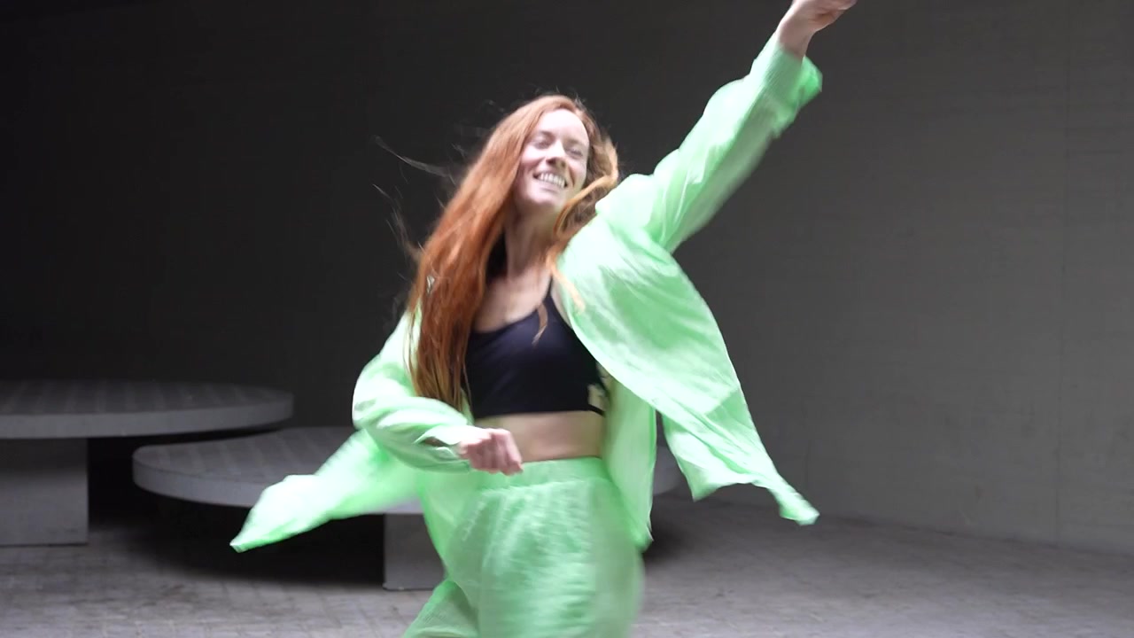 A lively youthful woman is energetically dancing indoors clad in a vibrant green attire