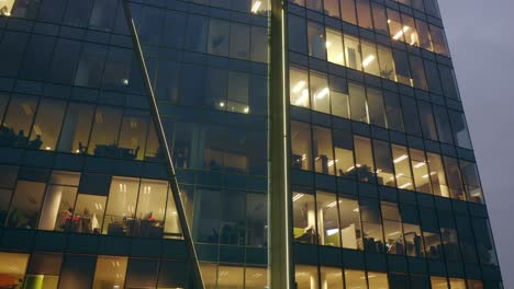 cinematic view from a drone of a night skyscraper with office windows and business people working at computers late at night.