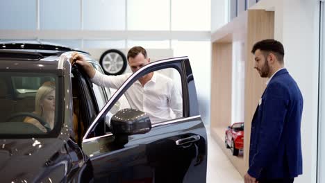 Blonde-woman-sitting-in-driver's-seat-while-her-husband-talking-to-a-sale-consultant