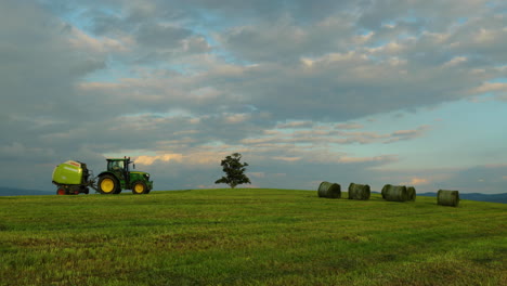 una máquina agrícola montada en el heno de carga en el suelo en una colina con vistas a las nubes en movimiento y cambiando la luz del sol a la sombra con vistas al paisaje natural en 4k 60fps