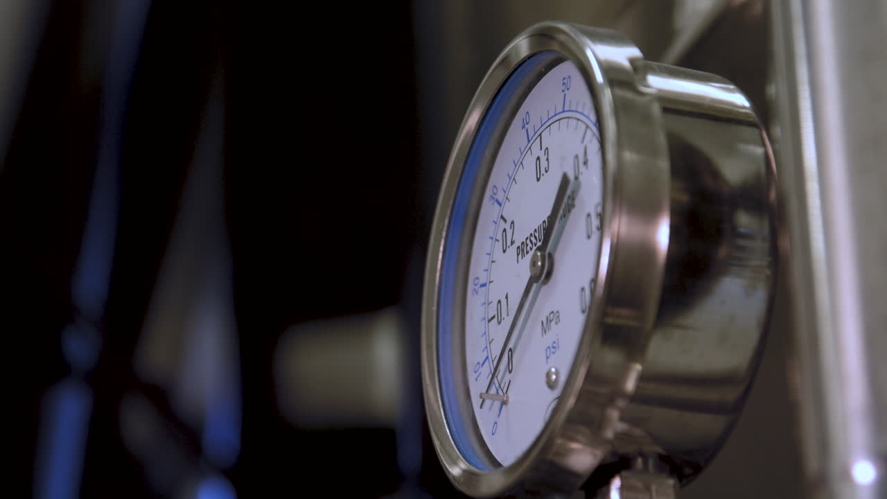 Closeup shot of pressure gauge mounted on a stainless steel fermentation tank in a brewery, ending in focused background view