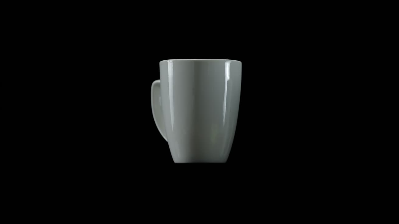 Scatto in studio minimale di una tazza in ceramica bianca che ruota lentamente su sfondo nero per un'esposizione pulita del prodotto.