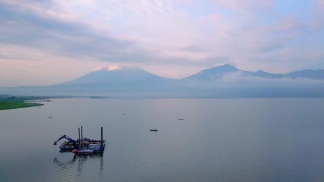 flyover view of indonesia lake with digger boat and mountains in background