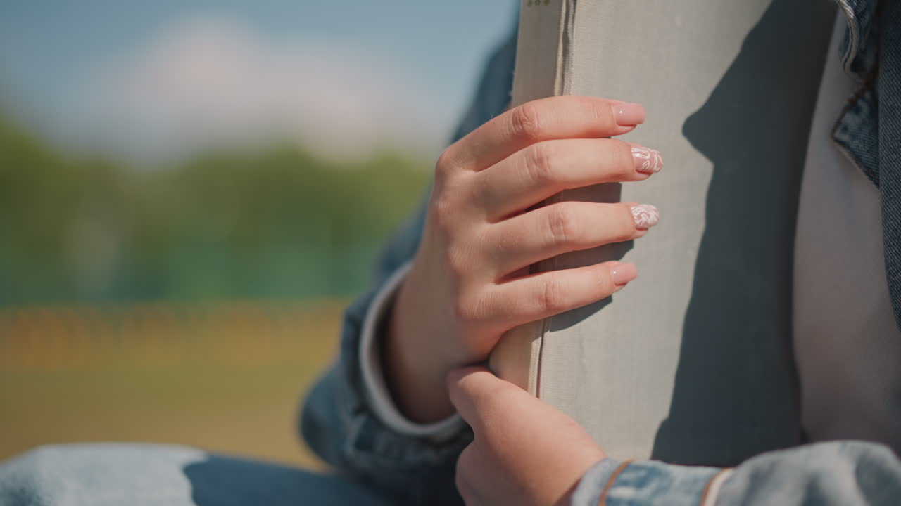Immagine dettagliata di mani che tengono un libro con grazia. Focus sulle mani che afferrano il libro con una raffinata nail art. Rappresentazione intima di mani ben curate che stringono un libro con precisione ed eleganza