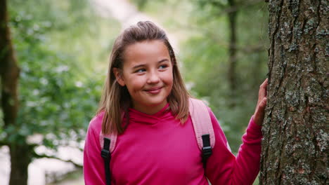 A-girl-standing-between-trees-in-a-forest,-looking-around,-close-up,-Lake-District,-UK