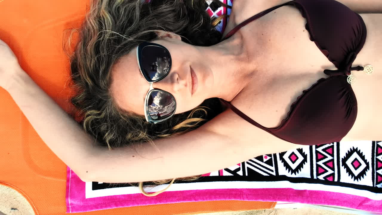 Young woman sitting on the beach sand near water and relaxing. Top view. Slow motion