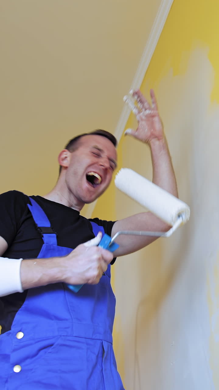 Man having fun during painting room. Professional young happy man with paint roller having fun
