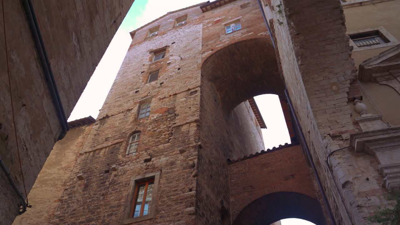 Arcate in pietra e luce solare che illumina uno stretto passaggio nella Perugia medievale