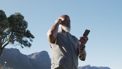 Senior-african-american-man-exercising-using-smartphone-putting-earphones-in