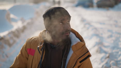 high angle view of photographer adjusting camera strap while standing on snowy urban sidewalk with pedestrians passing, exhaling visible breath into crisp frosty morning air under pale winter sky