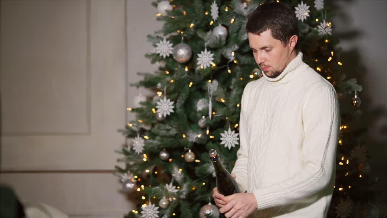 Man opening champagne bottle near Christmas tree