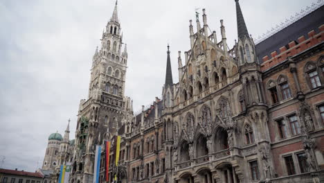 a closer look at the intricate neo-gothic facade of the new town hall (neues rathaus) at marienplatz, munich, with the frauenkirche’s iconic domes in the background.