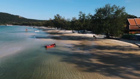 man on a scooter drives away from the speedboat that has just docked on the sandy beach of koh rong sanloem in cambodia on a clear sunny day