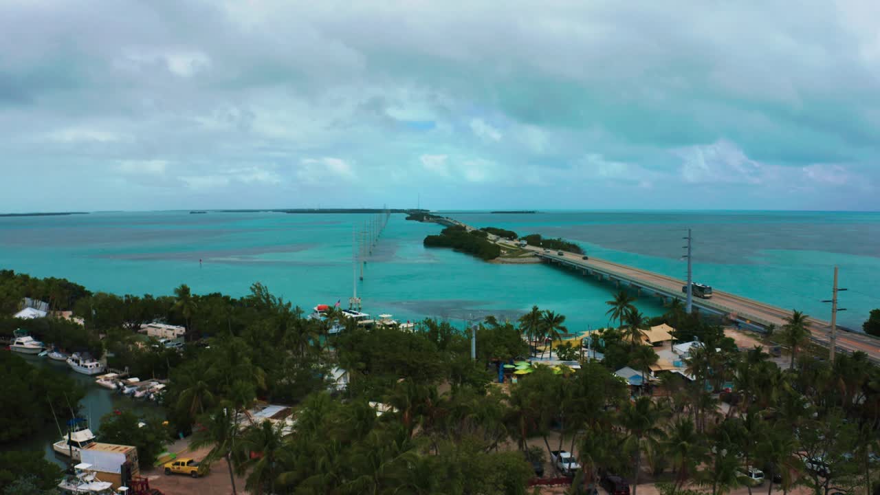 Aerial 4K UHD drone footage of palm trees next to the Highway One leading from Miami all the way down to Key West in Florida. The turquoise Atlantic Ocean is surrounding coral reef islands