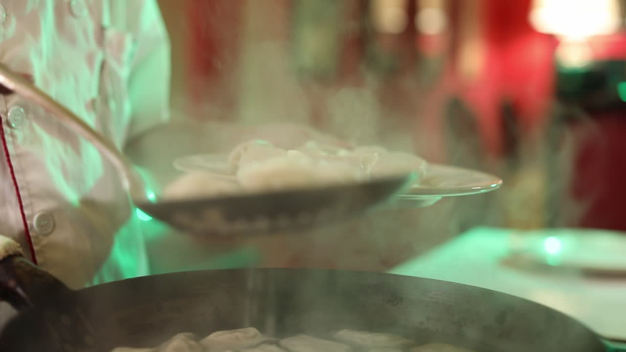 Close up shot of a professional chef scooping freshly boiled dumplings on to a plate