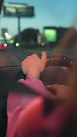 dama vista desde atrás conduciendo por la noche con las luces de la calle reflejadas en ella y la carretera, otros coches son visibles con sus luces encendidas, ligeramente borrosas, mientras un coche pasa por su lado