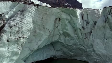 big glacier in the italian alps with cave and glacial green lake, aerial bottom to top shot